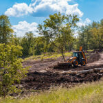 Bulldozer clearing land with fallen trees in a rural area for site preparation on a sunny day.
